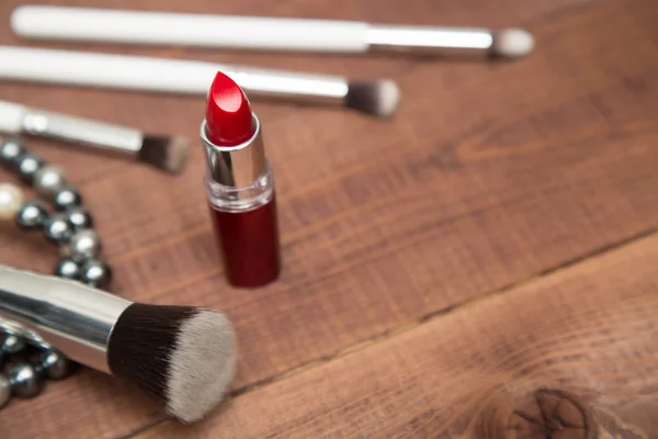 Artículos de maquillaje pinceles y lápiz labial, esparcidos por una superficie de madera —  Fotos de Stock