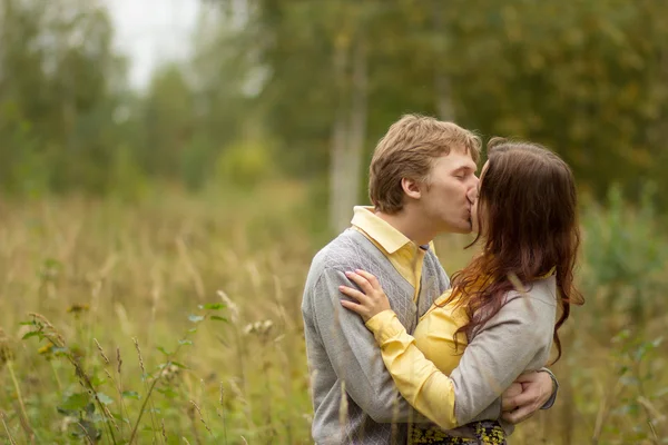 Νεαρό ζευγάρι με κίτρινο και γκρι ρούχα φιλιά στο πάρκο — Φωτογραφία Αρχείου