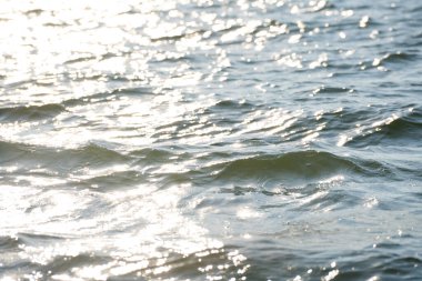 Güneş ışığı, yumuşak su dalgalarının yüzeyinde parlıyor.