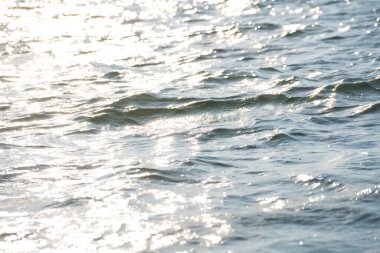 Güneş ışığı, yumuşak su dalgalarının yüzeyinde parlıyor.