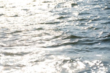 Güneş ışığı, yumuşak su dalgalarının yüzeyinde parlıyor.