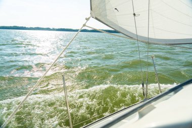 Sailing yacht cutting through waves on sunny lake
