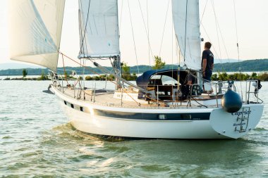 Sailing yacht with crew navigating on lake at sunset