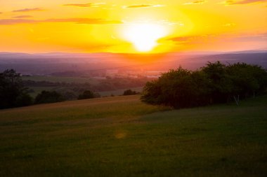 Ağaçlarla ve kırsal ufuk çizgisiyle çayırların üzerinde altın gün batımı