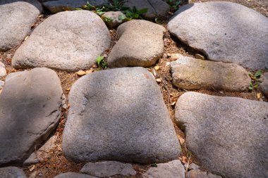 Çevrede küçük çakıl taşları, toprak ve orman enkazı ile çevrili kırsal bir yol oluşturan büyük doğal taş levhaların yakın görüntüsü..
