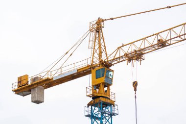 Santral kabini olan sarı vinç, bulutlu gökyüzüne karşı kanca ve karşı ağırlıklar. İnşaat alanlarında malzeme taşımak için kullanılan endüstriyel inşaat ekipmanları.