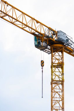 Bulutlu bir gökyüzüne karşı bir inşaat alanında sarı kule vinci. Sanayi kaldırma ekipmanlarının santral kabini, kanca ve karşı ağırlıklar, inşaat, mühendislik ve kentsel kalkınma sembolü.
