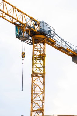 Bulutlu bir gökyüzüne karşı bir inşaat alanında sarı kule vinci. Sanayi kaldırma ekipmanlarının santral kabini, kanca ve karşı ağırlıklar, inşaat, mühendislik ve kentsel kalkınma sembolü.