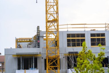 İnşaat halindeki bir binanın tepesinde bulutlu bir gökyüzüne karşı asılı kancalı sarı kule vinci. Kentsel inşaat alanında endüstriyel kaldırma ekipmanları.