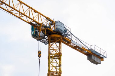 Bulutlu bir gökyüzüne karşı bir inşaat alanında sarı kule vinci. Sanayi kaldırma ekipmanlarının santral kabini, kanca ve karşı ağırlıklar, inşaat, mühendislik ve kentsel kalkınma sembolü.