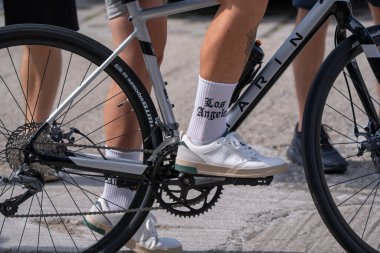 Modern bir yol bisikletiyle ayakta duran bisikletlinin yakın çekimi. Motosiklet çerçevesi, araba yağmuru, beyaz spor ayakkabılar ve spor şehir taşıma konseptini gösteren ayrıntılı şehir yaşam tarzı sahnesi.