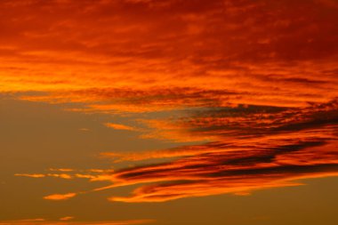 Akşam gökyüzünde parlayan dramatik kırmızı ve turuncu günbatımı bulutları. Yoğun sıcak renklere ve canlı doğal ışığa sahip ateşli atmosferik bulutlar.