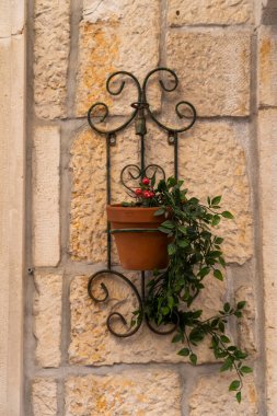 Süslü bir metal duvar tutacağında süslü bir terasotta saksısı kırsal bir taşa karşı, büyüleyici Akdeniz detayı.