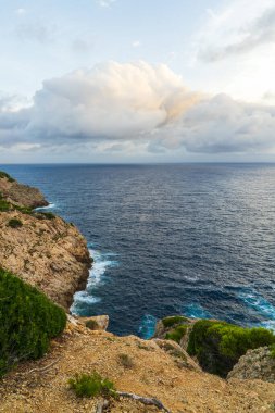 İspanya 'nın Mallorca adasında derin mavi deniz manzaralı kayalık bir sahil. Akdeniz manzarası, bulutlu gökyüzü, doğal güzellik. Mükemmel seyahat hedefi.