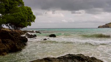 Şiddetli deniz dalgaları fırtınadan önce dramatik bir gri gökyüzü altında kayalık bir kıyı şeridine çarpar. Mallorca, Balearic Adaları, İspanya.