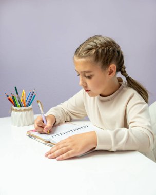 Masada oturan ve evdeki deftere yazan küçük bir kız. Samimi öğrenme ortamı çocukluk, evde eğitim, eğitim, yaratıcılık, konsantrasyon konuları için mükemmeldir..