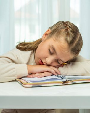 Genç öğrenci evde çalışırken uyuya kaldı, kafası kollarında dinleniyordu. Sahne çocukluk yorgunluğunu, okul stresini, sağlıklı bir rutine ihtiyaç duymayı taşır..