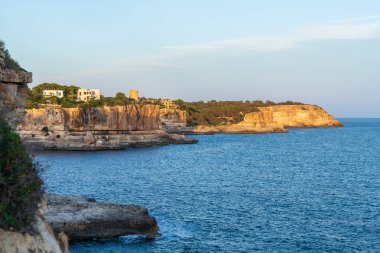 Mallorca 'nın Cala Santanyi kentinin kıyı manzarasında Akdeniz kıyısındaki kayalık kayalıklardaki tarihi gözlem kulesi yer alıyor. Resimli İspanyol kasabası ve dramatik kıyı şeridi.