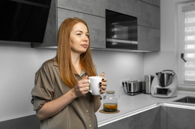 Evdeki sessiz mutfakta sabah çayından hoşlanan tatlı bir kadın. Huzurlu bir aile sabahı, rahat bir atmosfer, rahat bir yaşam tarzı, rahat bir ev, günlük ev zamanı..