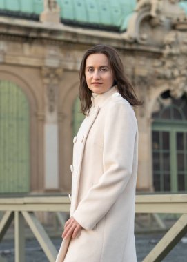 Beyaz önlüklü hoş, gülümseyen genç bir kadın kameraya bakıyor. Doğal ışık, sakin atmosfer, modern sokak tarzı, pozitif ruh hali..