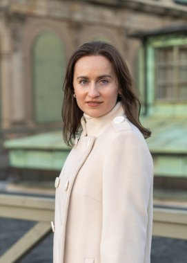 Beyaz önlüklü hoş, gülümseyen genç bir kadın kameraya bakıyor. Doğal ışık, sakin atmosfer, modern sokak tarzı, pozitif ruh hali..