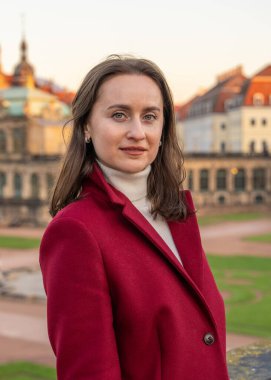 Açık havada kırmızı ceket giyen şık genç bir kadının portresi. Doğal ışık, modern şehir tarzı, atmosferik sokak fotoğrafçılığı.