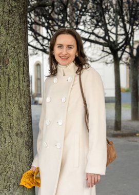 Sarı sonbahar yaprakları tutan, açık havada mevsimlik atmosferin tadını çıkaran, açık renk ceketli zarif genç bir kadın. Sıcak renkler, yaşam tarzı, sonbahar havası.