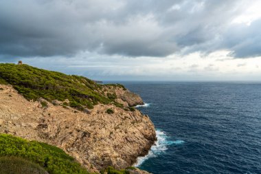 Far de Capdepera, Mallorca yakınlarındaki gri fırtına bulutları altında kayalık kıyı şeridine çarpan dalgaların dramatik görüntüsü. Doğa gücü kavramı, deniz manzarası, engebeli sahil..