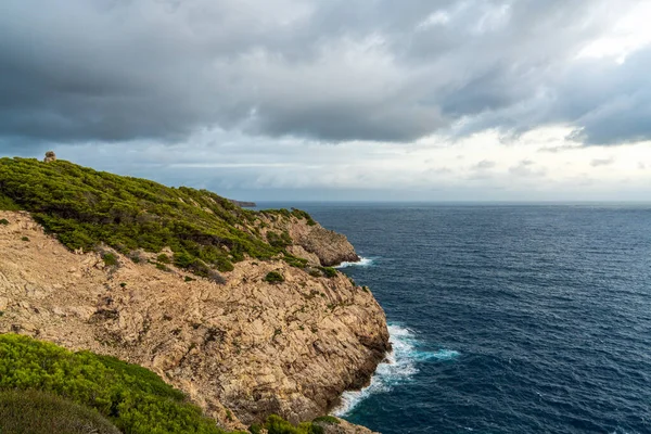 Far de Capdepera, Mallorca yakınlarındaki gri fırtına bulutları altında kayalık kıyı şeridine çarpan dalgaların dramatik görüntüsü. Doğa gücü kavramı, deniz manzarası, engebeli sahil..