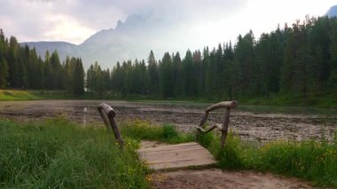 Yıllanmış ahşap köprü Antorno Gölü 'nü sembolik Drei Zinnen ile çerçeveliyor, Tre Cime di Lavaredo yükseliyor. Sakin alp suları, çarpan Dolomite tepeleri, sakin dağ ortamı.
