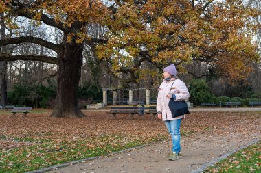 Sonbahar parkında yürüyen orta yaşlı bir kadın huzur ve sessizliğin tadını çıkarıyor. Rahatlama, kişisel bakım, yaşam tarzı ve açık hava eğlencesi kavramı.