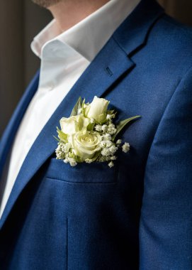 Beyaz gül yaka çiçekli mavi takım elbiseli şık bir damat. Düğün portresini kapat. Düğün, tören.