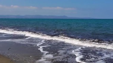 Kıbrıs 'ın güney kıyısındaki çakıl taşlı plajda deniz dalgaları yavaşça yuvarlanıyor. Doğal deniz manzarası, huzurlu kıyı atmosferi, yaz yolculuğu, sakin bir arka plan..