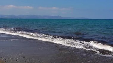 Kıbrıs 'ın güney kıyısındaki çakıl taşlı plajda deniz dalgaları yavaşça yuvarlanıyor. Doğal deniz manzarası, huzurlu kıyı atmosferi, yaz yolculuğu, sakin bir arka plan..