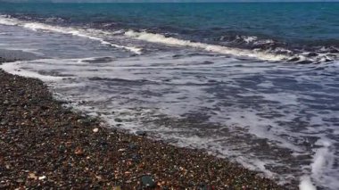 Deniz dalgaları Kıbrıs 'ın güney kıyısı boyunca çakıl taşlı bir kıyı şeridini yıkıyor. Sakin Akdeniz manzarası, rahatlatıcı deniz havası, yaz seyahati ve arka plan kullanımı için ideal.