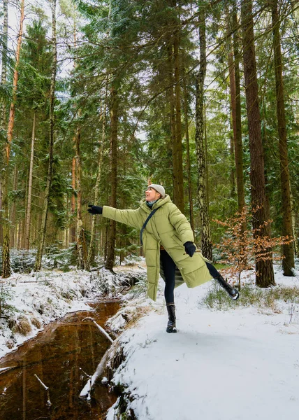 Sıcak kış kıyafetleri içinde mutlu genç bir kadın. Karlı ormanda tek bacağının üzerinde neşe içinde poz veriyor. Kollarını aç, parlak kahkahalar özgürlük, neşe, canlı kış atmosferi..