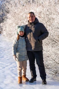 Gülümseyen baba kış orman yürüyüşü sırasında kızına sarılır. Arka planda buzla kaplı ağaçlar. Aile bağları, hassas bağlar, soğuk doğada sıcaklık ve bakım.