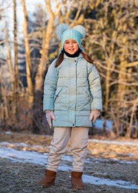 Karlı kış ormanlarında yürüyen, kalın giysili şirin küçük bir kız. Mutlu çocuk doğayı seviyor, soğuk mevsim açık hava aktivitesi, çocukluk sevinci, huzurlu kış manzarası.