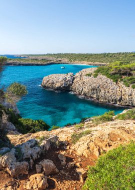 Kalo Blanc, Mallorca, İspanya 'da engebeli kıyı şeridi tarafından açık turkuaz denize demirlenmiş bir yat. Akdeniz yaz manzarası, seyahat yeri ve tatil konsepti.