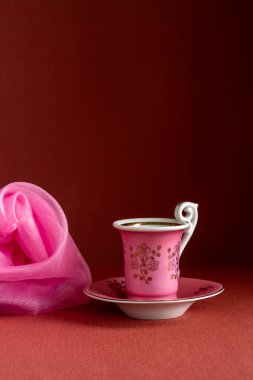 Küçük pembe kupa ve kahverengi arka planda pembe şalla sakin bir hayat. Minimum kompozisyon rahat ruh hali, yumuşak renkler, zarif dekoratif stil.