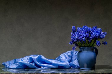 Büyük mavi muscari buketi, ablue vazosu ve açık mavi şalla mermer masanın üzerinde koyu arka planda. Kopya alanı olan zarif çiçek kompozisyonu.