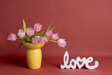 Pembe laleler, sarı vazolar ve beyaz aşk harfleriyle dolu bahar yaşamı. Fotokopi alanı olan Pastel romantik arka plan. Düğün kırtasiyesi, tebrik kartları ve pazarlama için ideal.