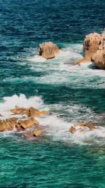 Turkuaz Akdeniz dalgaları Mallorca, İspanya 'daki Cala Agulla' da kayalık kıyı şeridine çarpıyor. Kristal berrak suyla popüler yaz seyahatleri, turizm için mükemmel. Dikey.