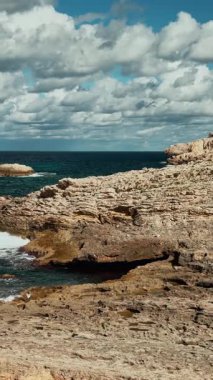 Kıyı dalgalarının kayalık sahile beyaz deniz köpüğüyle çarptığı dikey bir video. Doğal Akdeniz kıyısı İspanya, Mallorca 'da Cala Agulla' yı ele geçirdi. Mükemmel seyahat, doğa geçmişi..