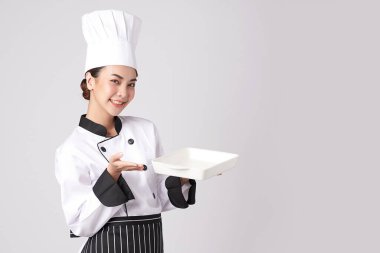 Güzel Asyalı kadın şef beyaz arka planda boş beyaz tabak tutuyor..