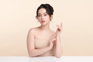 Güzel, genç bir Asyalı kadın, bej bir arka planda temiz, taze bir ten. Cilt bakımı, yüz bakımı, kozmetoloji, güzellik ve kaplıca. Asyalı bir kadının zarif bir portresi..