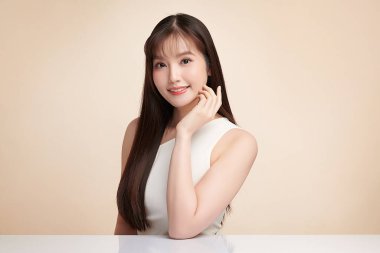 Güzel, genç bir Asyalı kadın, bej bir arka planda temiz, taze bir ten. Cilt bakımı, yüz bakımı, kozmetoloji, güzellik ve kaplıca. Asyalı bir kadının zarif bir portresi..