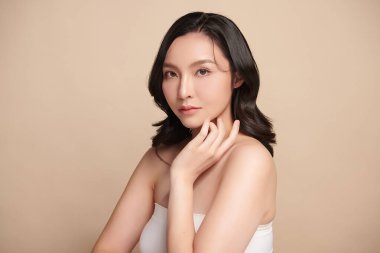 Güzel, genç bir Asyalı kadın, bej bir arka planda temiz, taze bir ten. Cilt bakımı, yüz bakımı, kozmetoloji, güzellik ve kaplıca. Asyalı bir kadının zarif bir portresi..