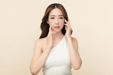 Güzel, genç bir Asyalı kadın, bej bir arka planda temiz, taze bir ten. Cilt bakımı, yüz bakımı, kozmetoloji, güzellik ve kaplıca. Asyalı bir kadının zarif bir portresi..