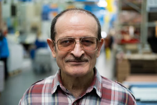 A grown man with a mustache, glasses, and a plaid shirt looks at the camera